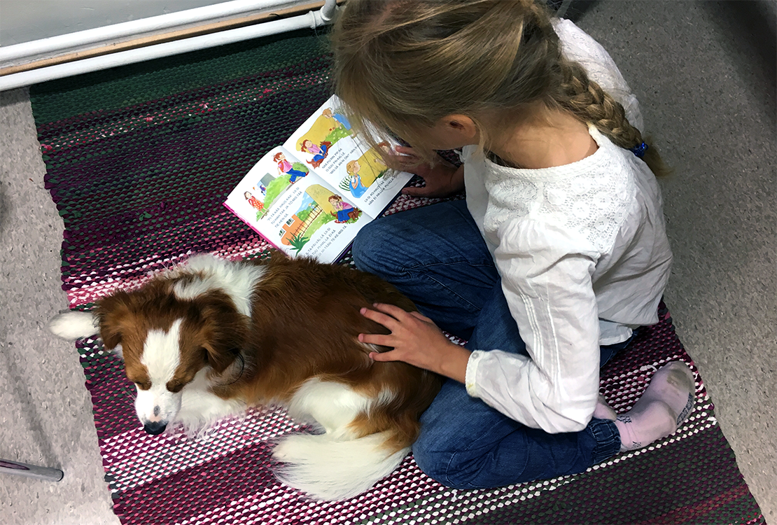 Tyttö lukee kirjaa Edske-koiran kanssa.