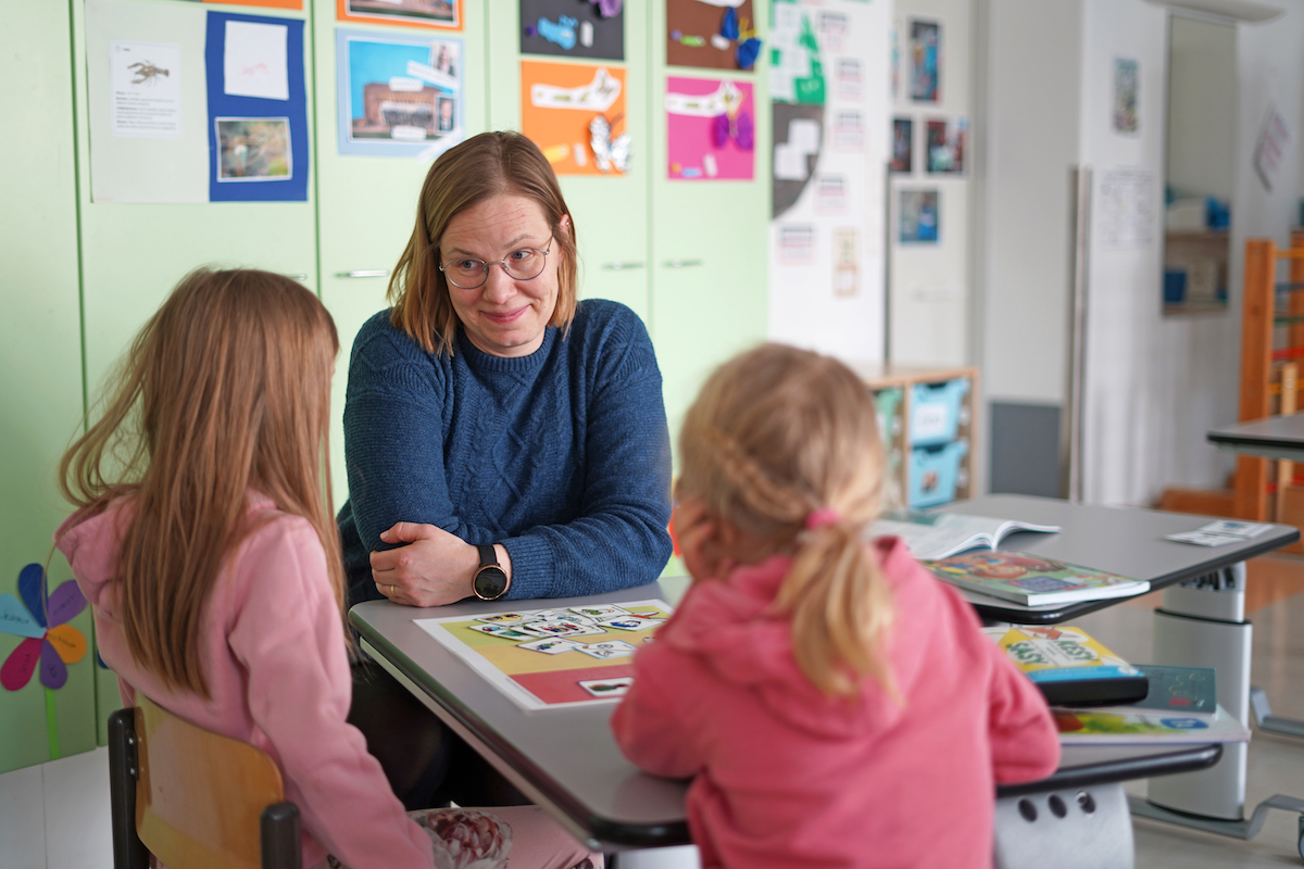 Oppimis- ja ohjauskeskus Valterin konsultoiva ohjaaja Henni Huttunen istuu pöydän ääressä kahden lapsen kanssa. Pöydällä on KESY-kuvakortteja levitettynä.